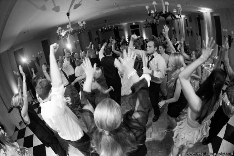 Wedding guests dancing with raised hands on crowded dance floor during lively wedding reception celebration