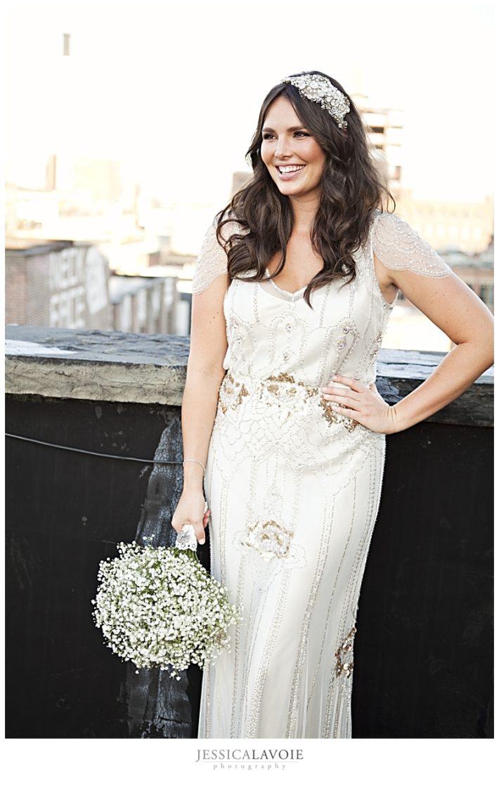 Bride posing on rooftop in beaded wedding gown holding bouquet