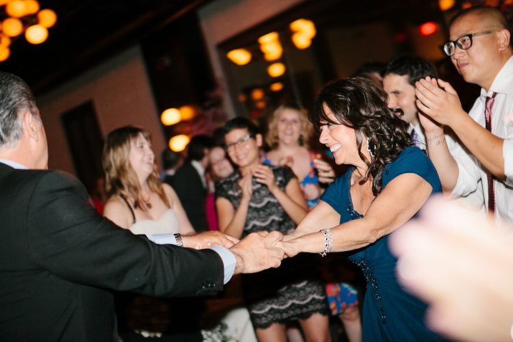Woman dancing joyfully with guests cheering around her at wedding reception