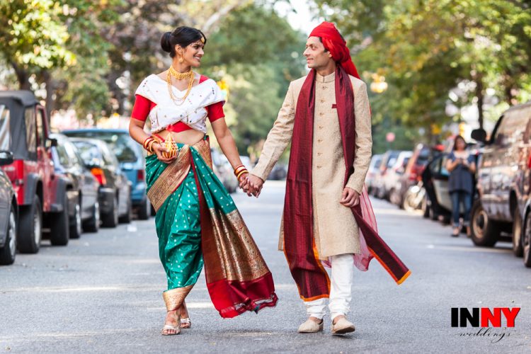 Couple in colorful traditional wedding attire walking hand in hand down city street