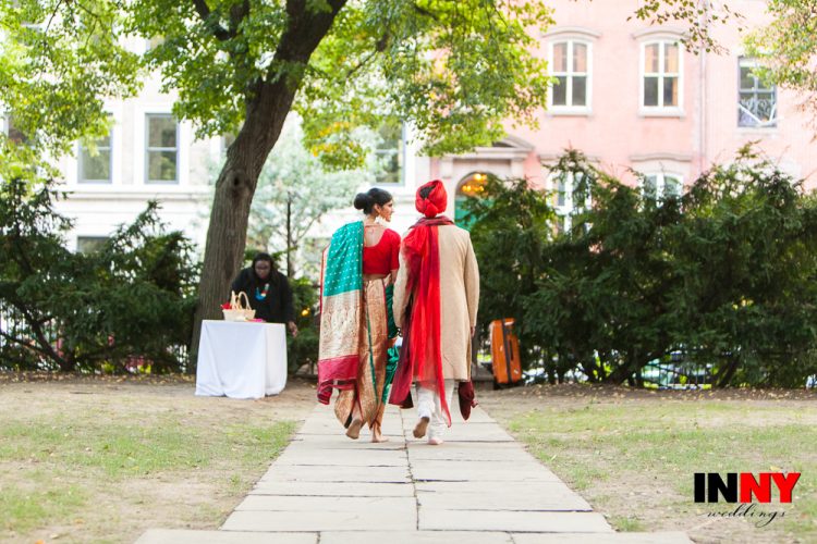 Couple in traditional attire walking hand in hand through outdoor garden path