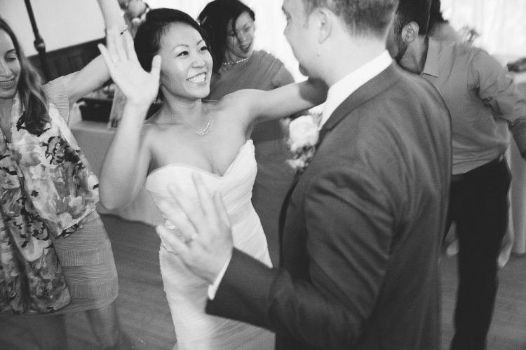 Bride dancing with groom while guests celebrate on reception dance floor