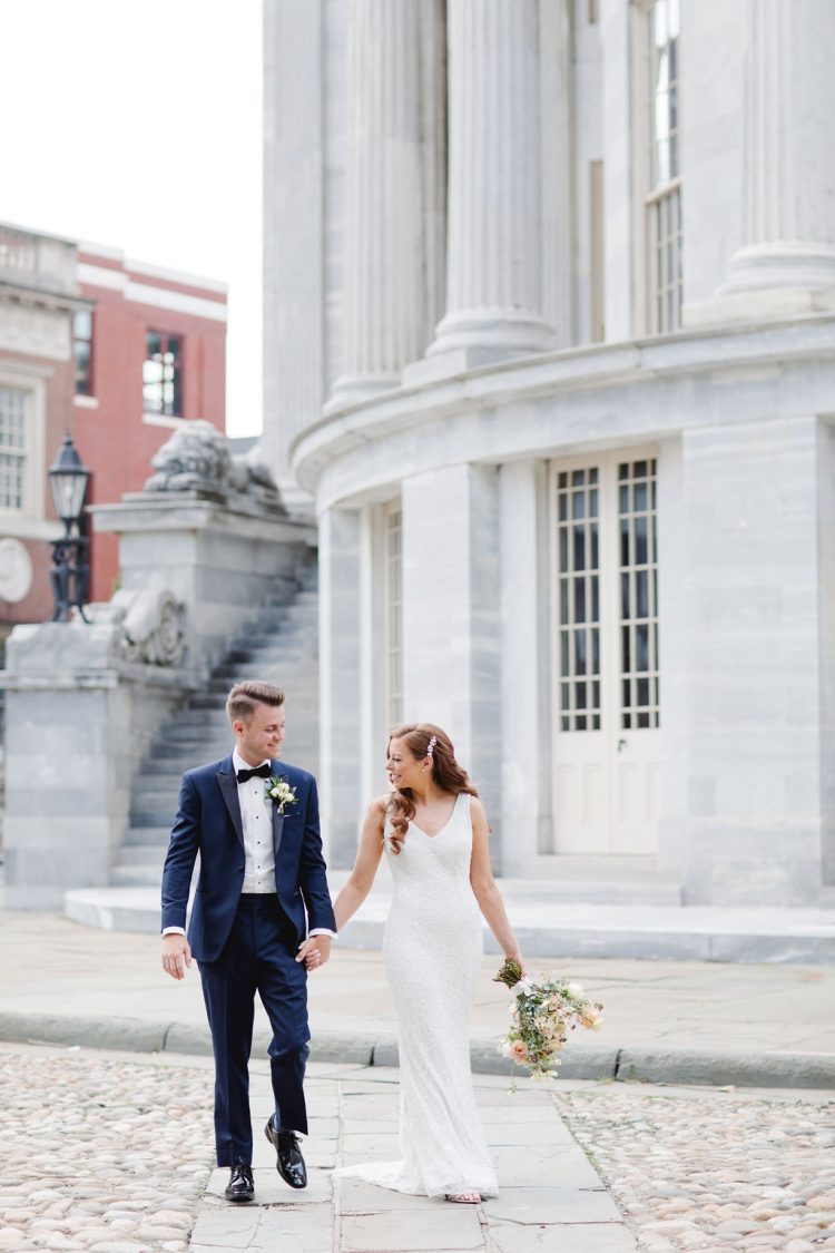 Bride and groom holding hands walking outside grand stone building at Downtown Club by Cescaphe