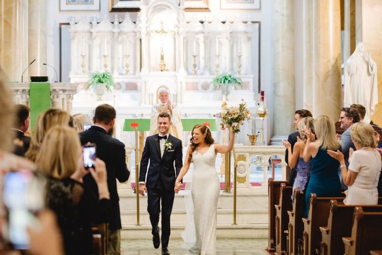 Bride and groom walking down church aisle as guests applaud