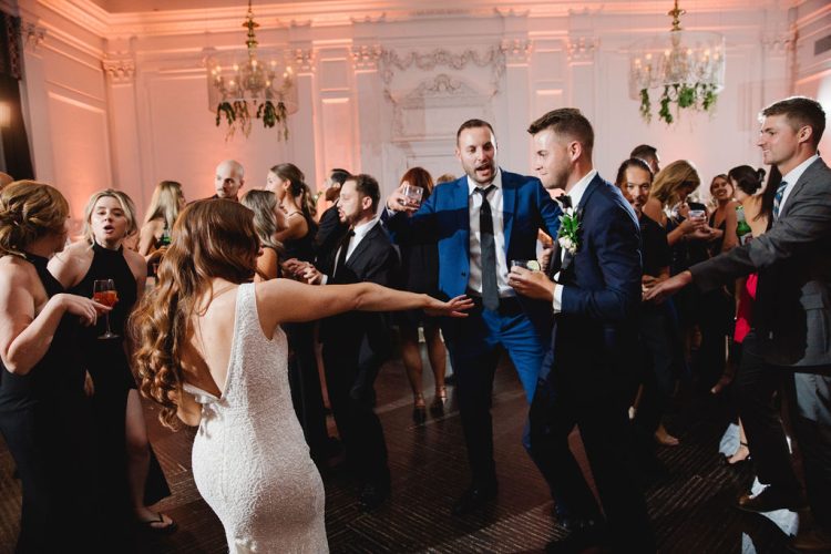 Bride dancing with guests on crowded reception dance floor in elegant ballroom