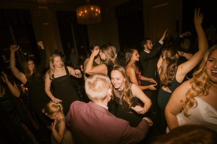Guests dancing closely together on crowded reception dance floor under warm lighting