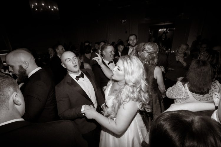 Guests dancing closely together on crowded reception dance floor in low light