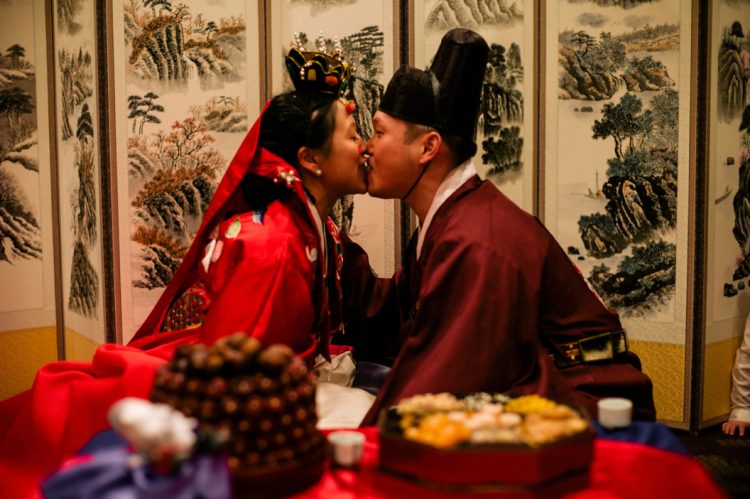 Couple sharing kiss during traditional Korean wedding ceremony while dressed in ceremonial hanbok attire