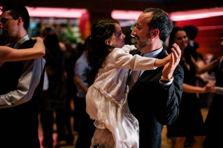 Man dancing with young girl during wedding reception while guests dance in background