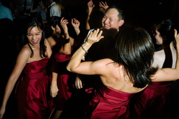 Wedding guests dancing enthusiastically together during lively reception celebration on darkened dance floor