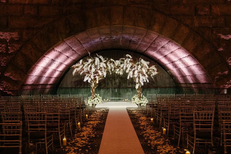 Indoor wedding ceremony aisle with floral arch and candle lighting at Guastavino’s