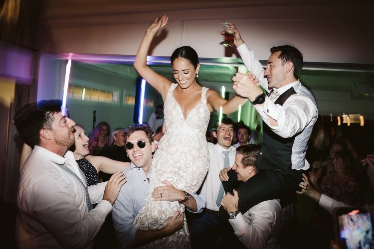 Bride and Groom lifted by guests on crowded wedding reception dance floor.