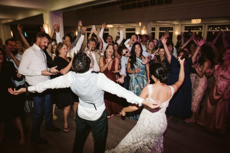 Bride and groom dancing surrounded by cheering guests on packed dance floor.