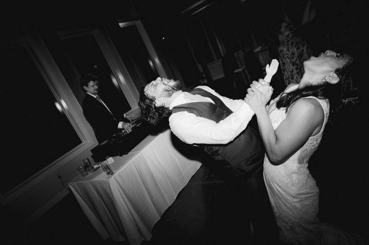 Bride and groom singing together on dance floor while wedding DJ performs in background.