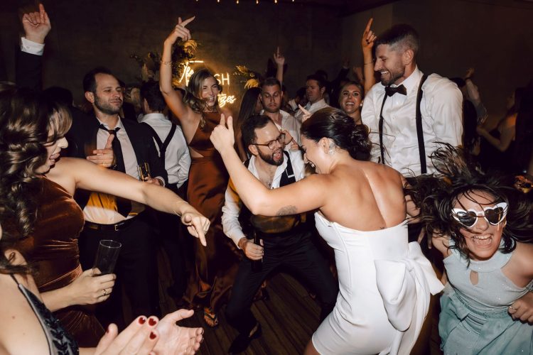 Bride and Groom dancing with guests on crowded wedding dance floor.