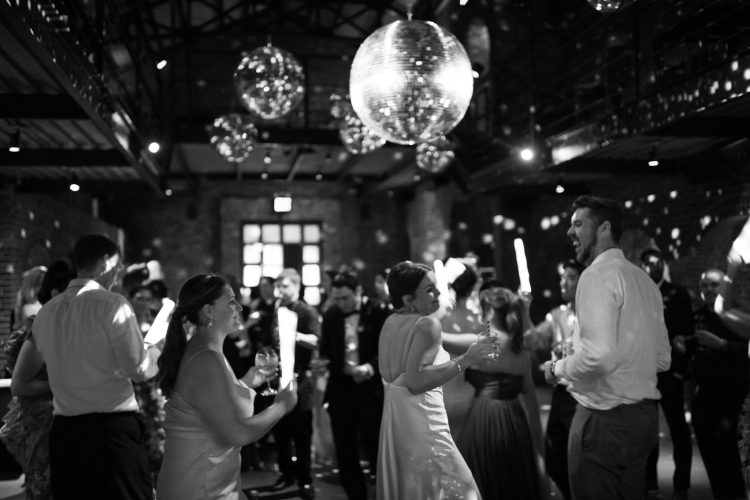 Wedding guests dancing under disco balls on crowded dance floor.