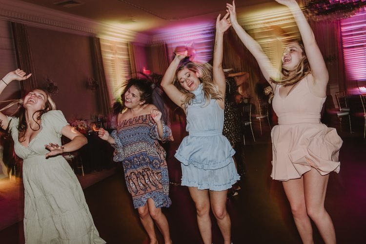 Wedding guests dancing with raised hands during lively dance floor moment.