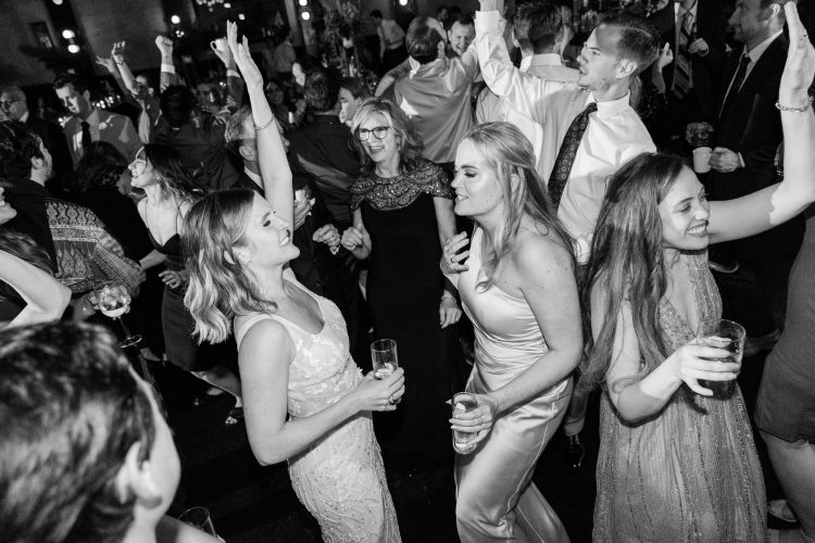 Bride dancing with friends on crowded wedding dance floor.