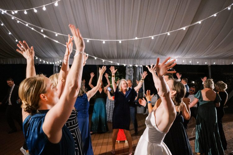 Wedding guests dancing with raised hands under string lights.