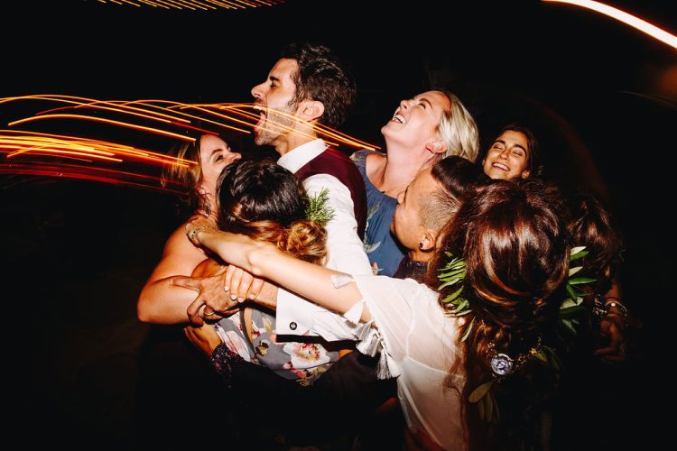 Bride and Groom hugging friends on lively wedding reception dance floor.