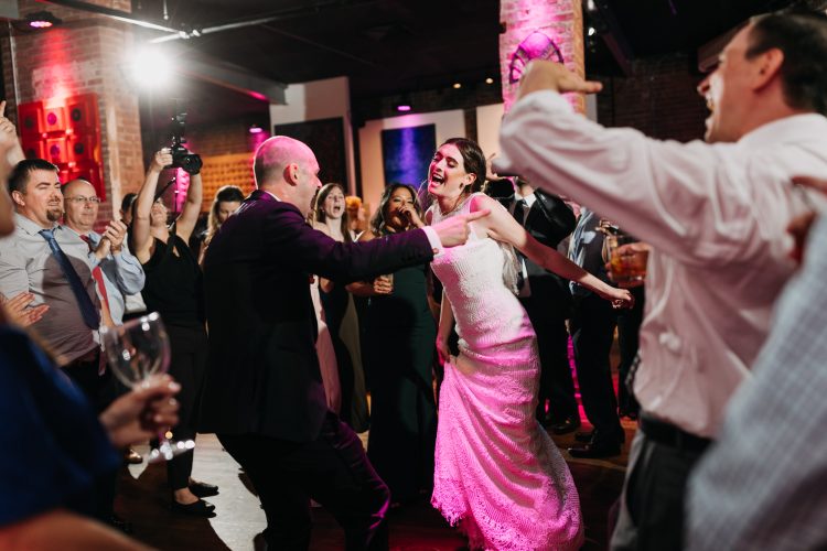 Bride singing with guests on crowded reception dance floor.