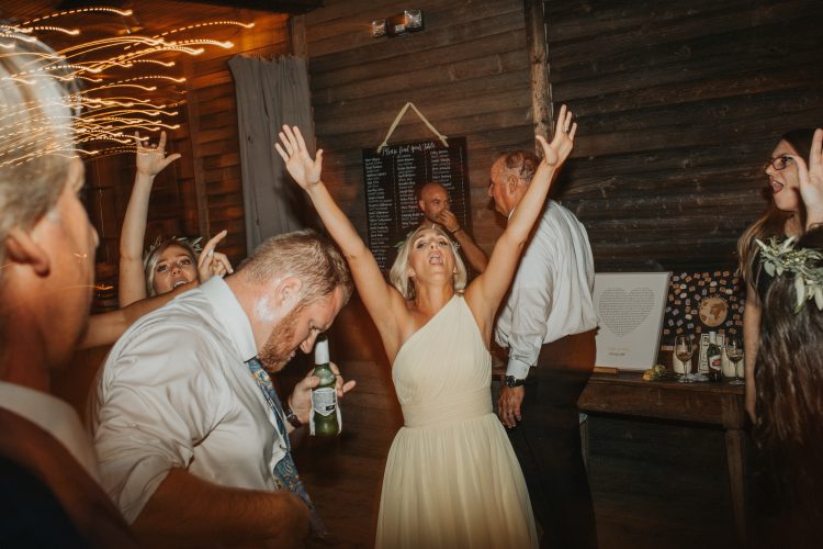 Wedding guests dancing with raised hands during reception celebration.