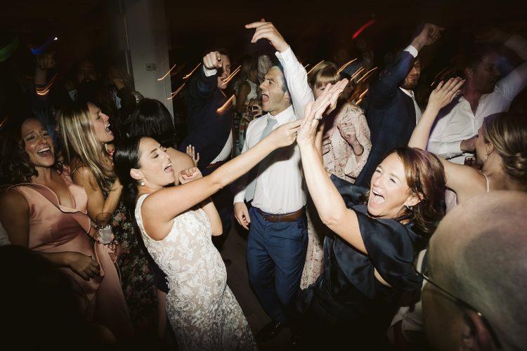 Bride dancing and high-fiving guest on crowded wedding dance floor.