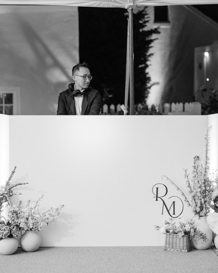 Wedding DJ performing behind white DJ booth at outdoor reception.