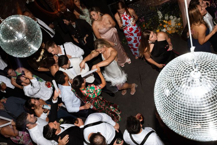 Overhead view of crowded wedding reception dance floor beneath disco balls.