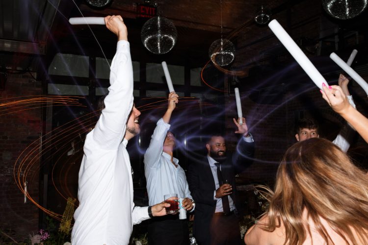 Wedding guests waving foam light sticks on reception dance floor.