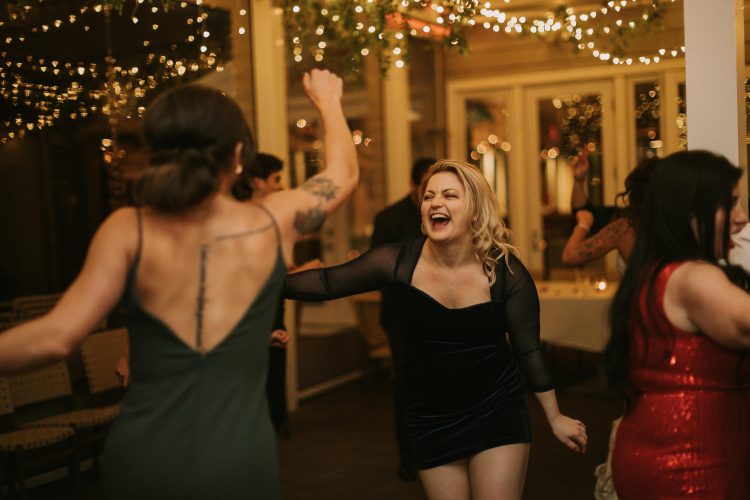 Guest laughing and dancing on the reception dance floor under string lights.
