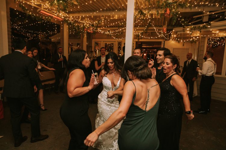 Bride dancing with friends under warm string lights at the reception.