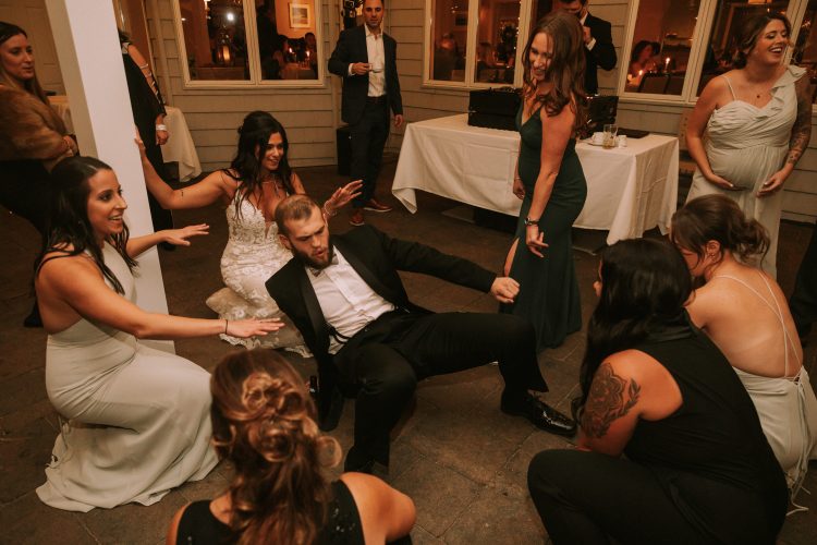 Groom showing off dance moves surrounded by cheering wedding guests.
