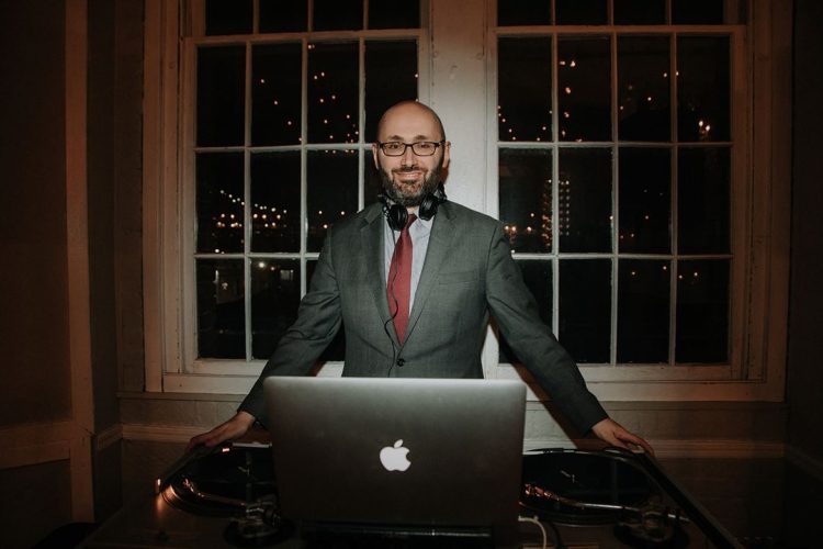 DJ standing behind a laptop and turntables at an event.