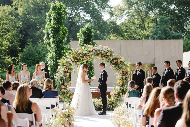 Bride and Groom standing under a floral arch during the ceremony.
