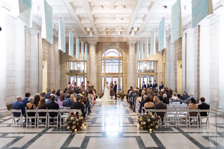 Large indoor wedding ceremony with guests seated on both sides.