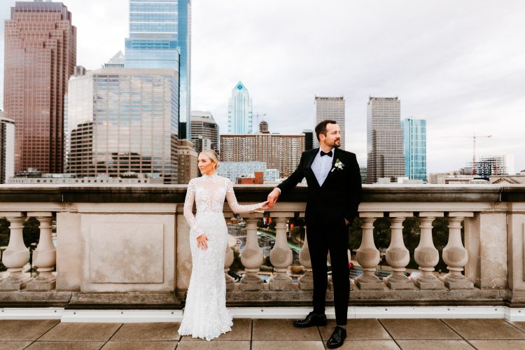 Bride and groom standing on a rooftop with a city skyline.
