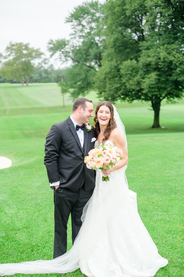 Bride and Groom standing together on a green lawn holding a bouquet.