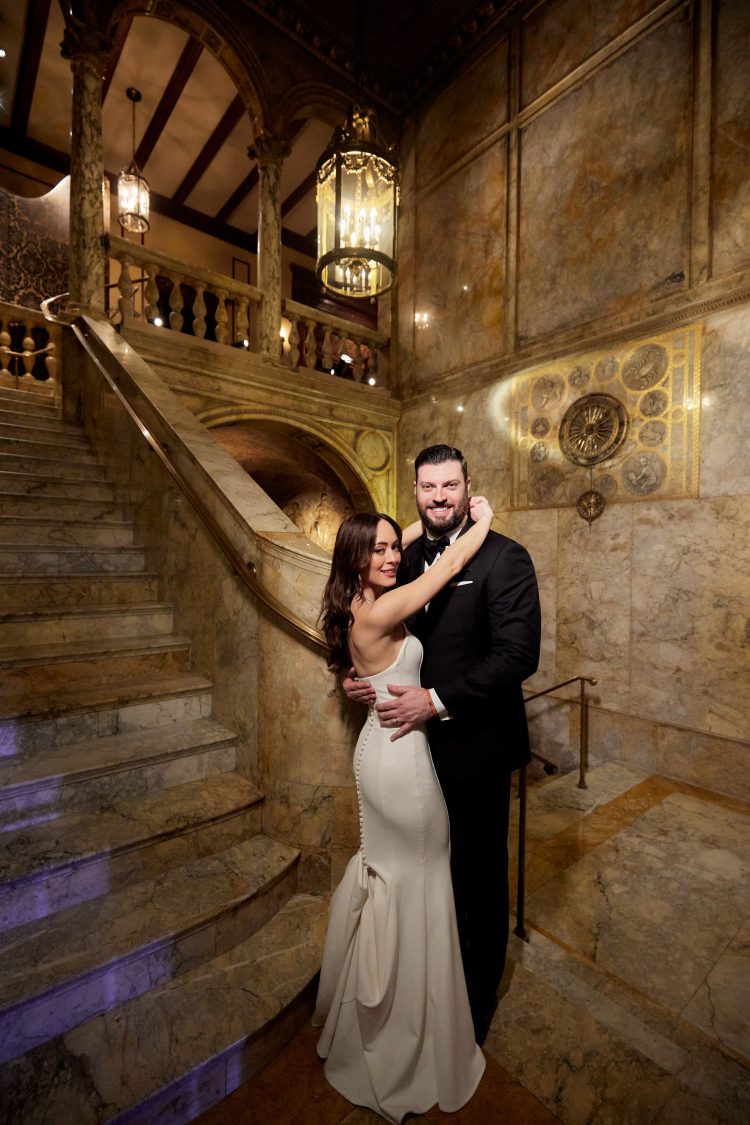 Bride and groom posing together by a grand staircase at Lotte New York Palace.