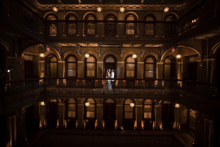 Bride and groom standing on a balcony in an elegant hall at The Beekman Hotel.