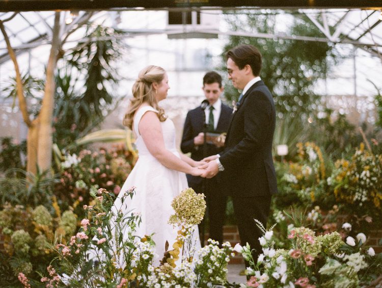 Bride and groom holding hands during a garden ceremony at Horticulture Center