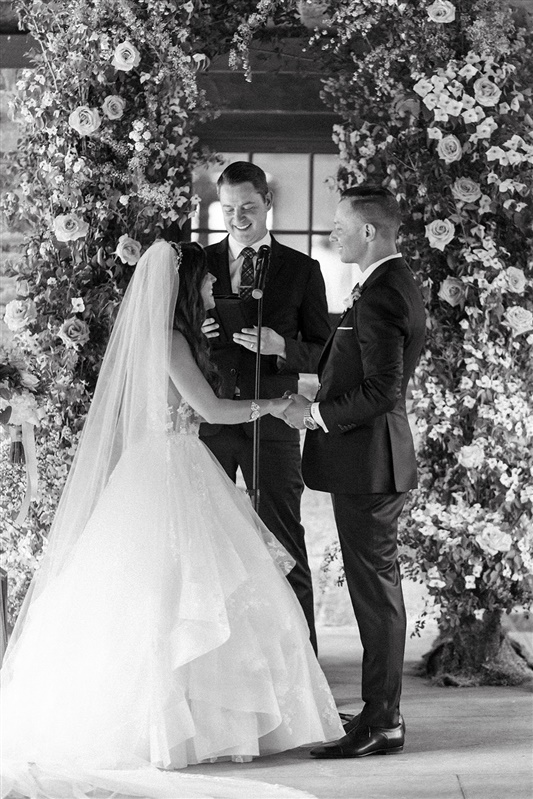 Couple holding hands beneath floral arch during wedding ceremony at Blue Hill at Stone Barn