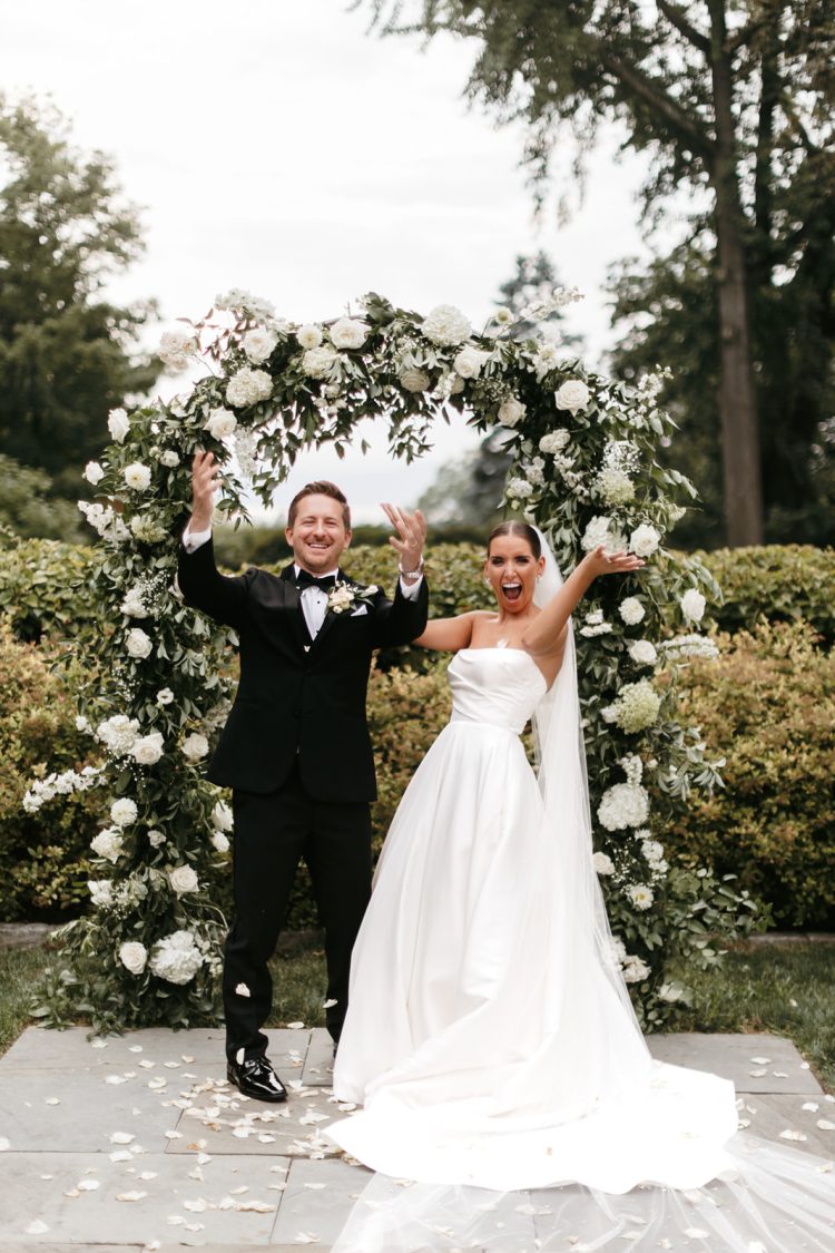 Bride and groom celebrating beneath floral wedding arch after ceremony at The Briarcliff Manor