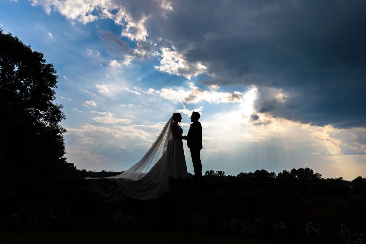 Bride and groom silhouette facing each other at sunset beneath dramatic sky at Le Chateau