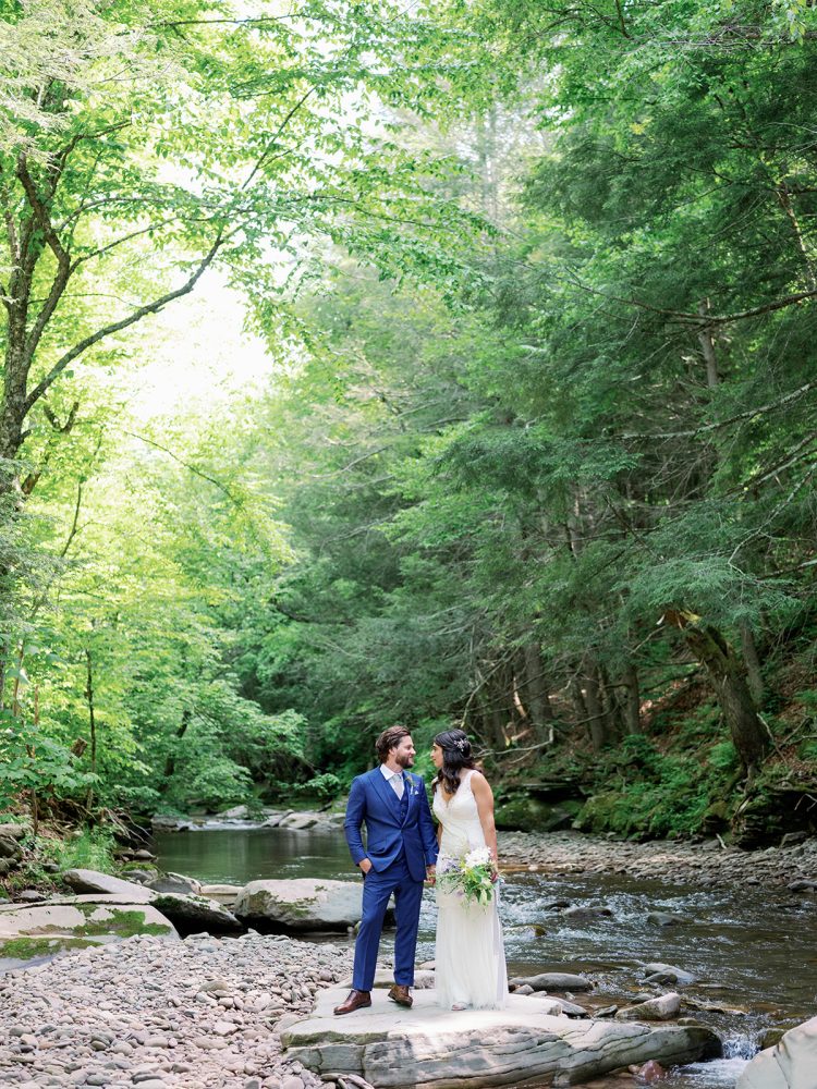 Bride and groom standing on rocks beside forest creek during outdoor wedding portraits at Full Moon Resort