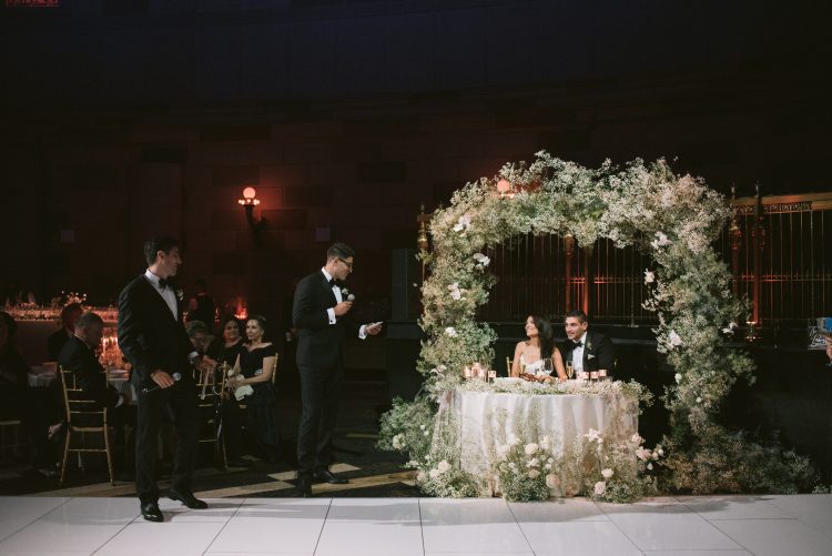 Wedding speech at sweetheart table under floral arch at Gotham Hall