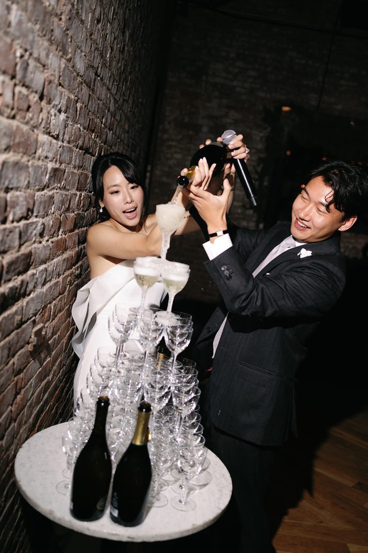 Bride and groom pouring champagne into stacked glass tower at Wythe Hotel