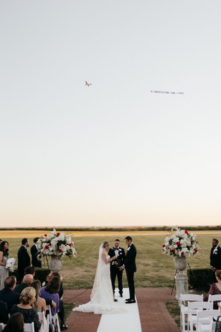 Outdoor wedding ceremony with plane flying banner overhead at Bourne Mansion