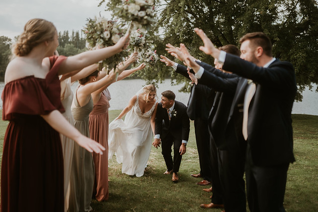Bride and groom running through cheering wedding party outdoors