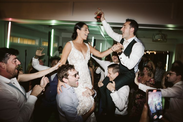Bride and groom lifted by guests while celebrating on the dance floor